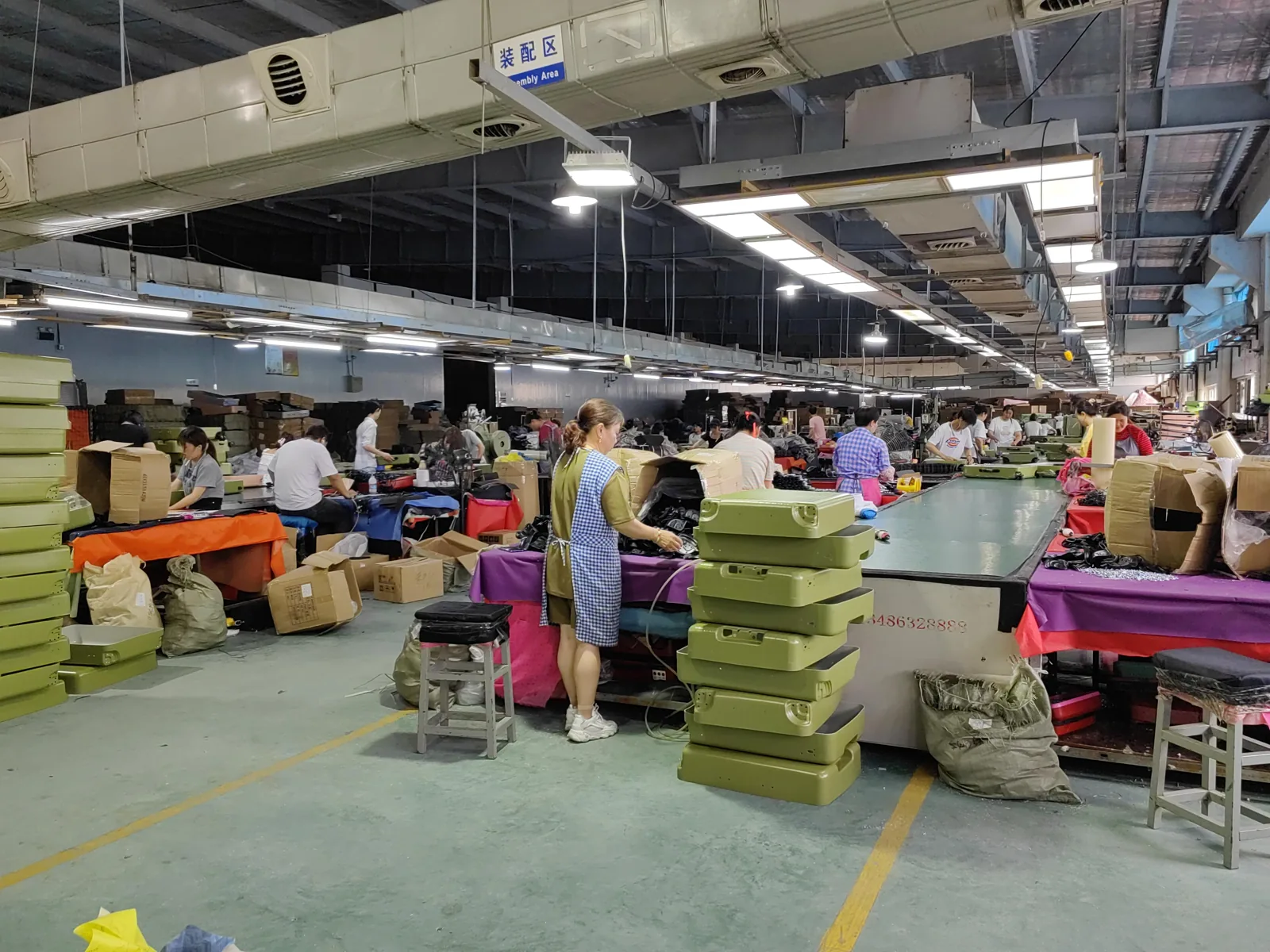 Assembly floor with stacked formed shells in the foreground and workers fitting components along long benches