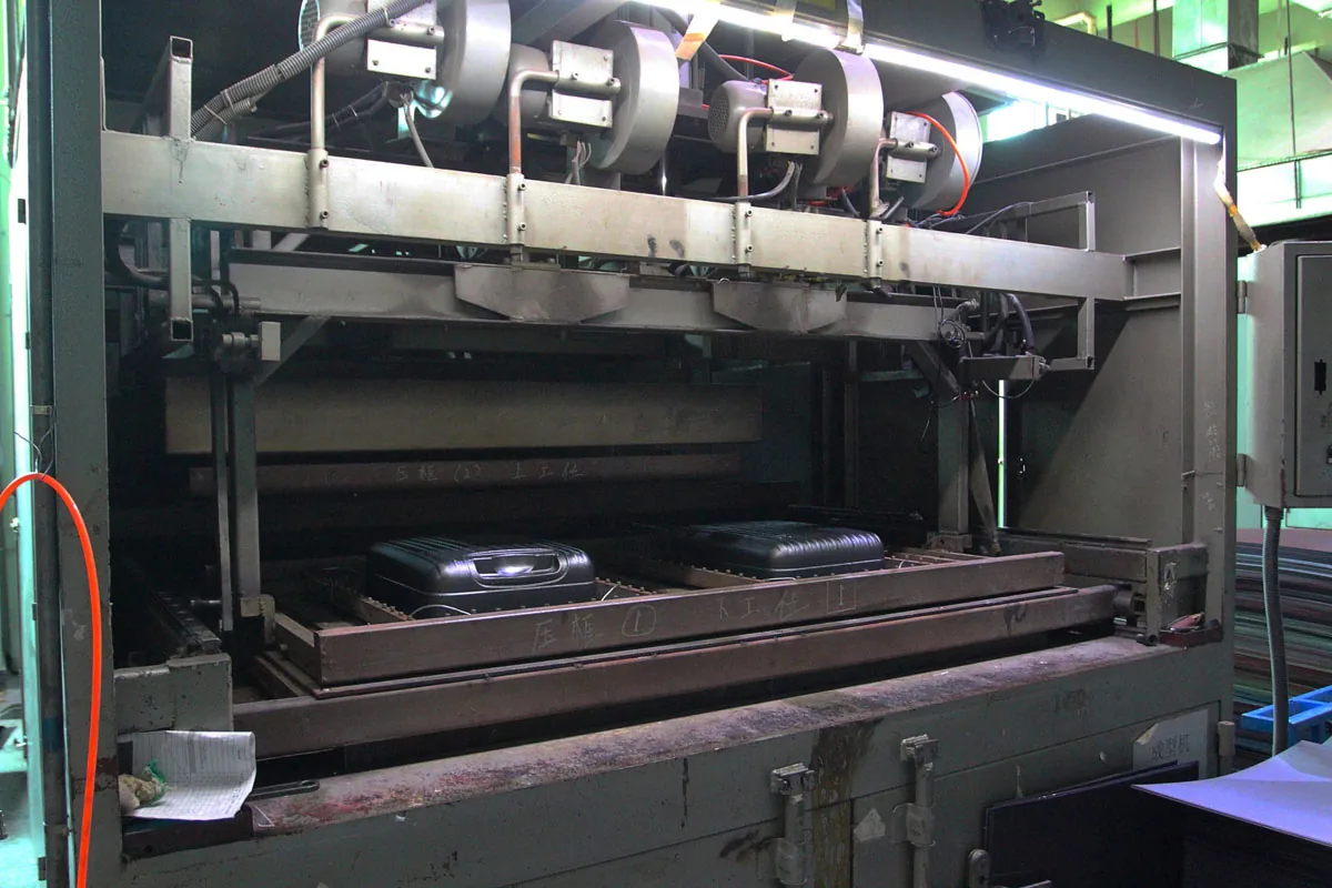 Large forming press with radiant heater banks above a tool holding two suitcase shells