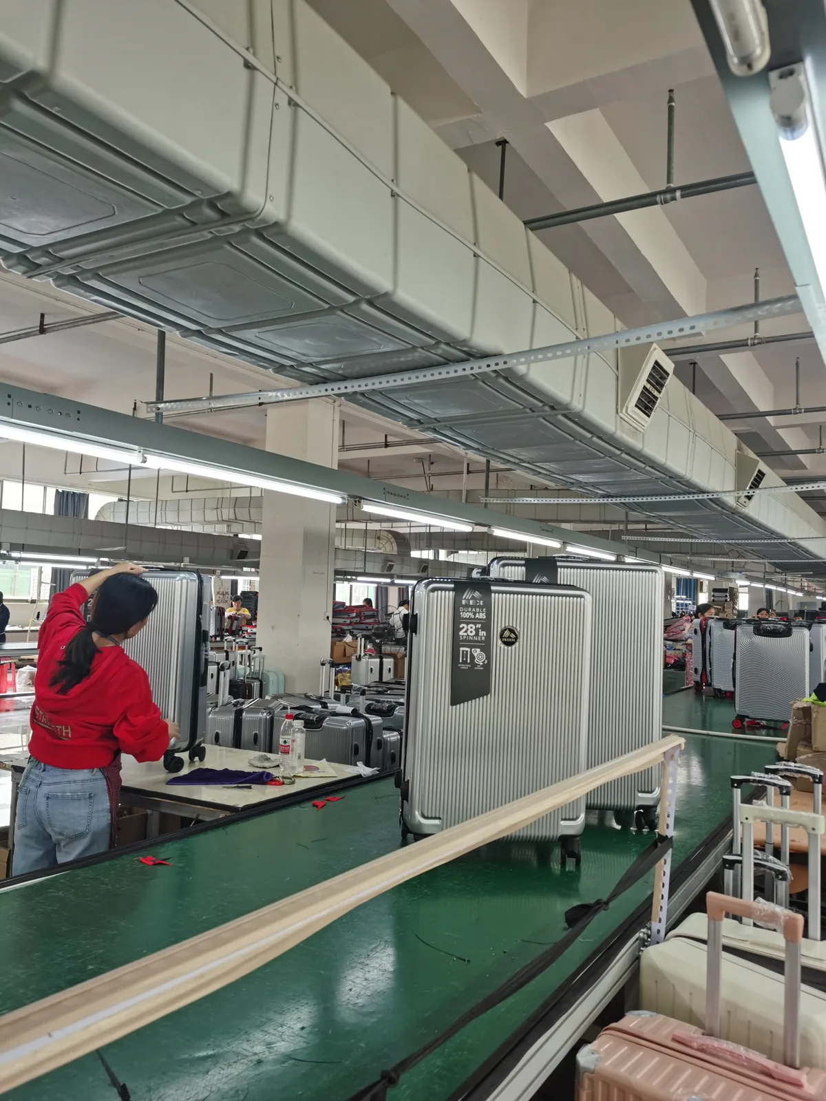 Finished suitcases moving along a green conveyor while a worker fits components at a side bench