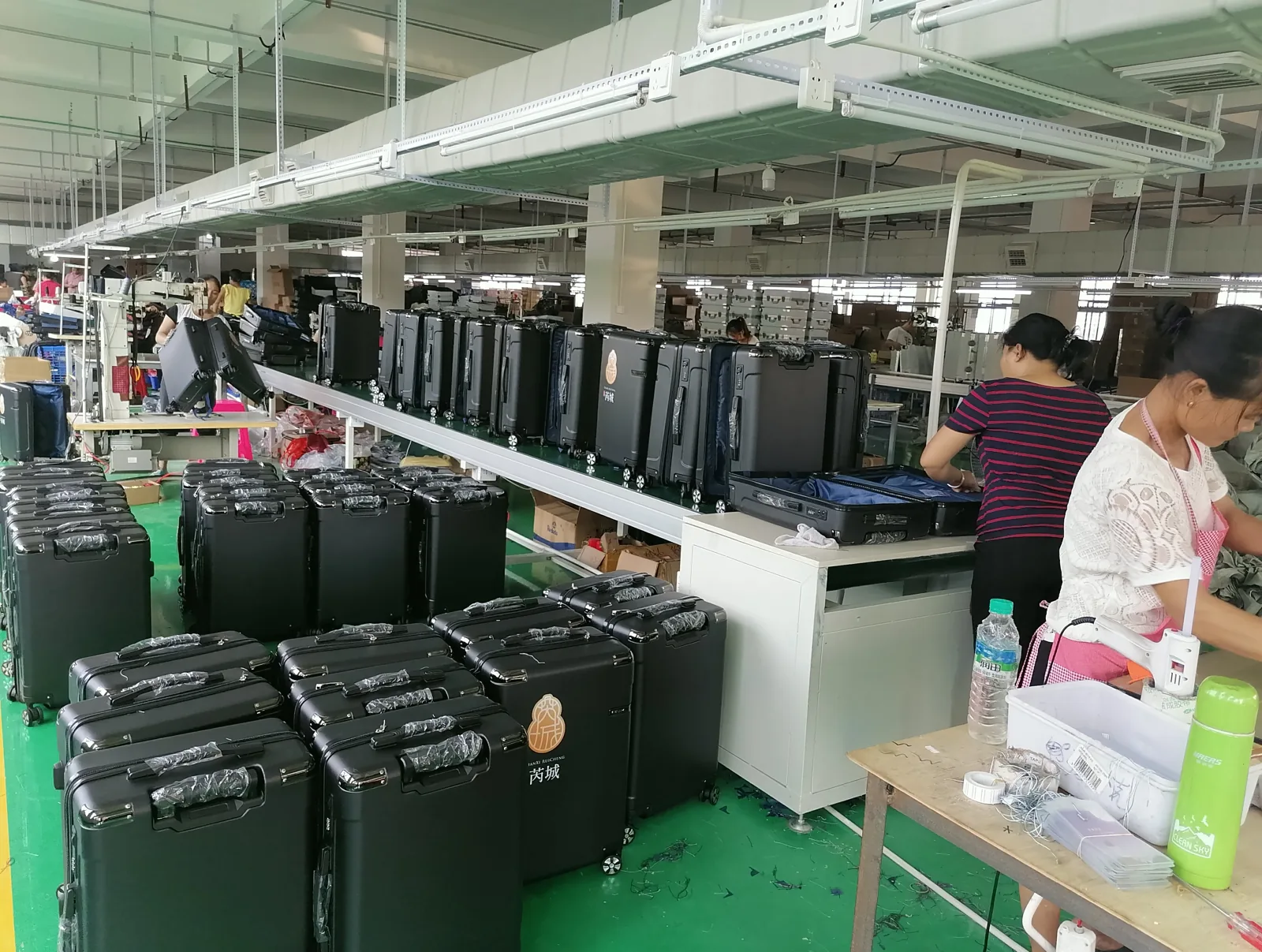 Rows of dark green frame cases stacked and moving along an assembly line with workers fitting interiors