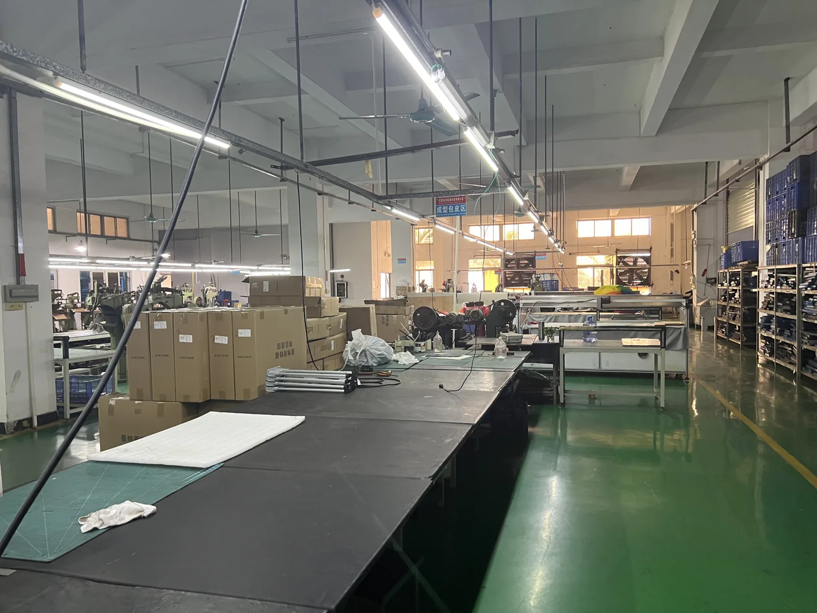 Long cutting tables with sewing machines behind and cartons of components stacked to one side