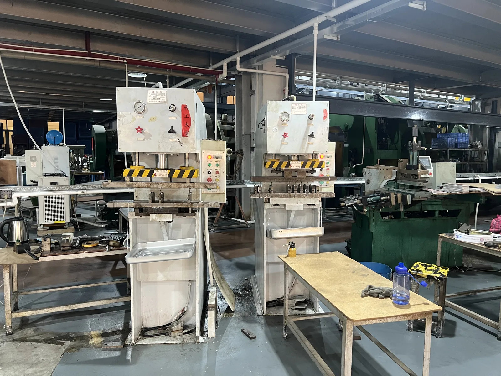 Two hydraulic presses forming aluminum luggage panels on the production floor