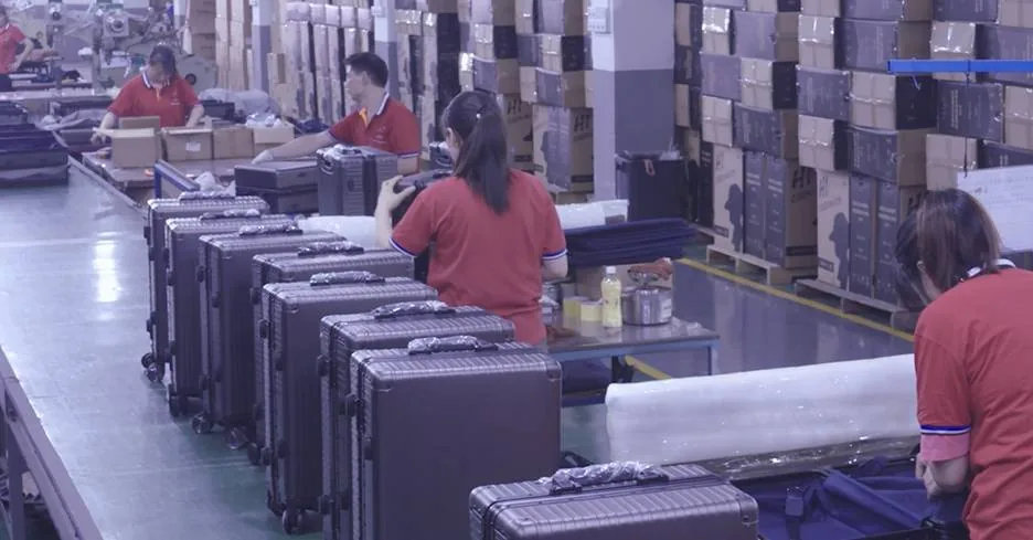 Finished aluminum frame cases moving along the packing line with rolls of protective film and stacks of printed export cartons behind