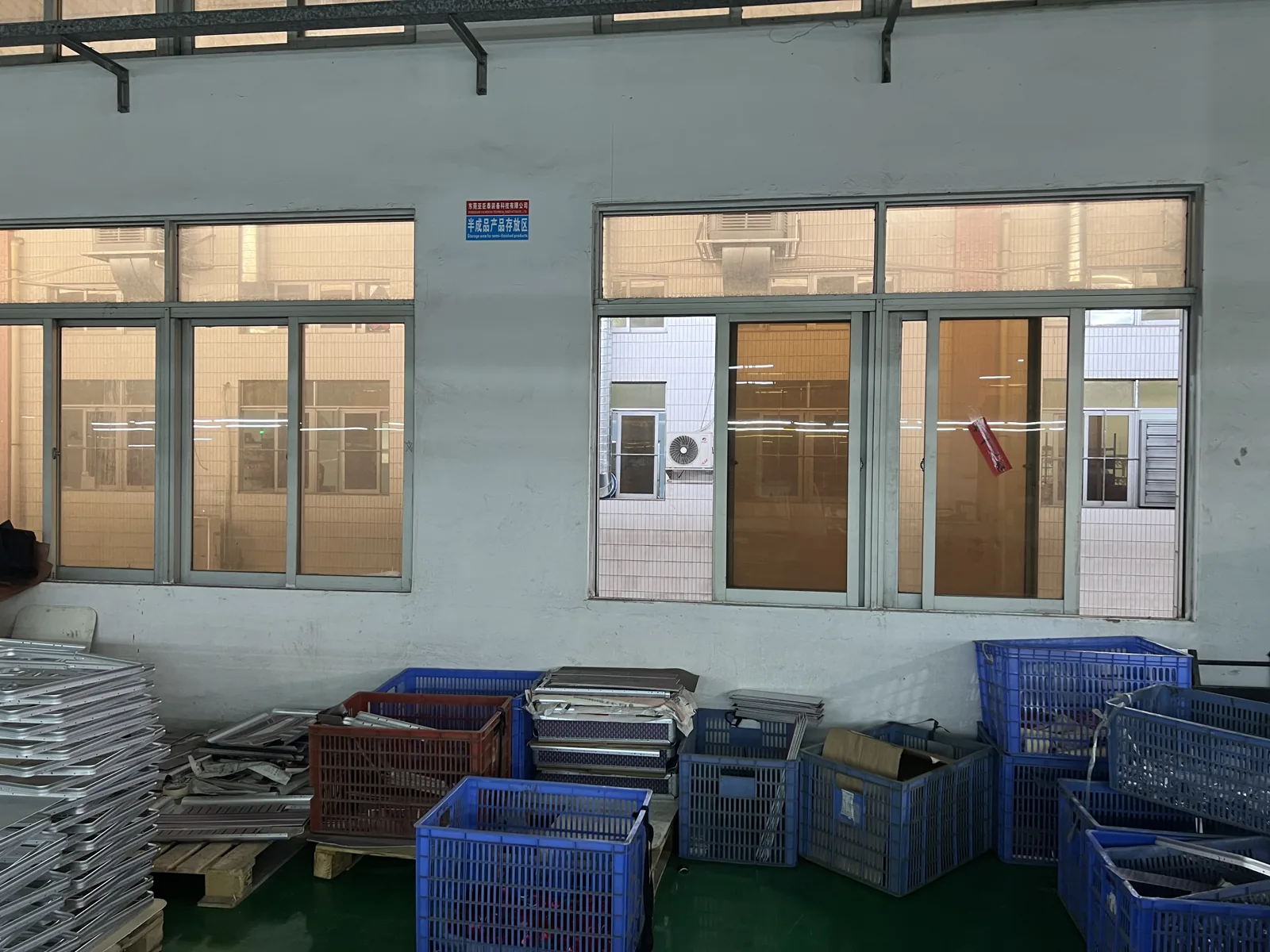 Stacked crates of cut aluminum frame components and panels on pallets beside a workshop wall