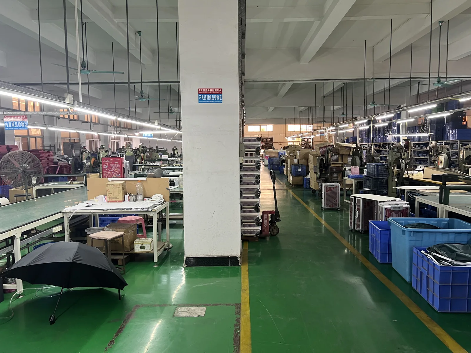 Sewing floor with rows of machines, a cart of aluminum frame profiles in the aisle and crates of cut panels