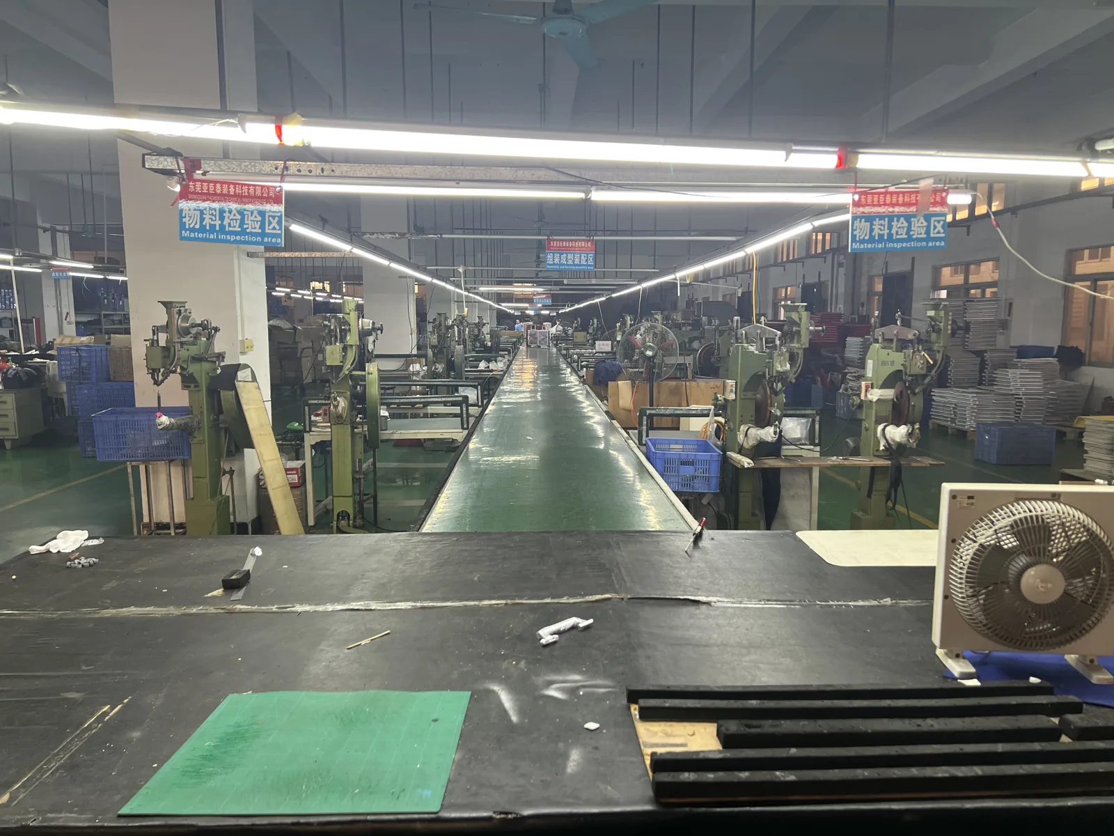 Long factory aisle lined with machines on both sides under material inspection area signs