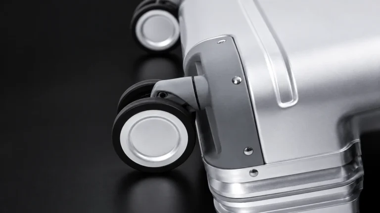 Close-up of a spinner wheel and corner guard on an aluminum suitcase, studio shot on black