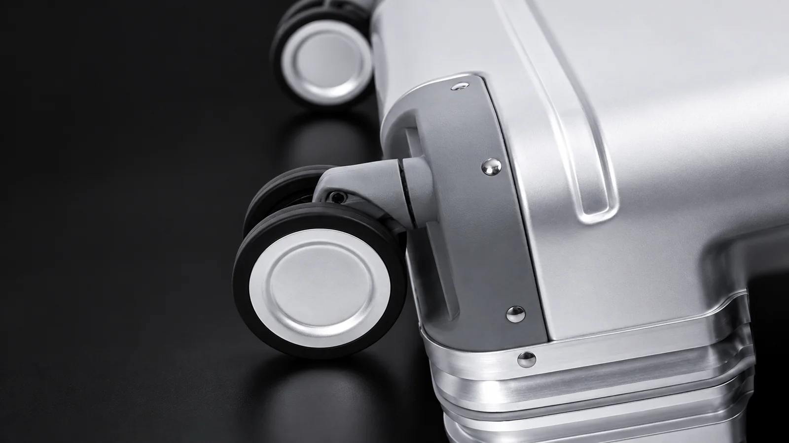 Close-up of a spinner wheel and corner guard on an aluminum suitcase, studio shot on black